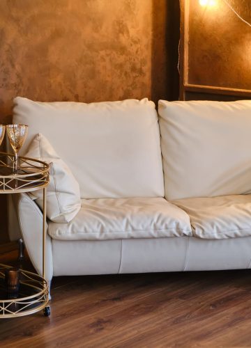 Empty comfy white couch, contemporary furniture inside of cozy living room interior with a garland of luminous lamps and a serving table on wheels. Wooden wall, brown laminate. Real estate