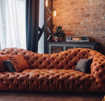 Modern fashionable red leather couch with cushions. Cropped Christmas tree. Brick wall. Loft design.
